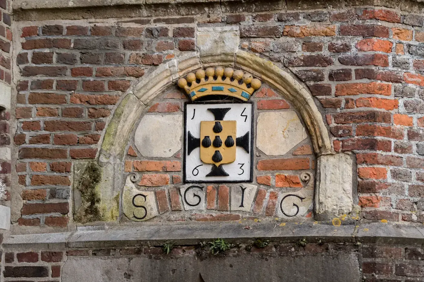 Ornate brick wall with a coat of arms featuring a crown, black symbols on a shield, and the year 1463. Initials "S.G.I.C." are below.
